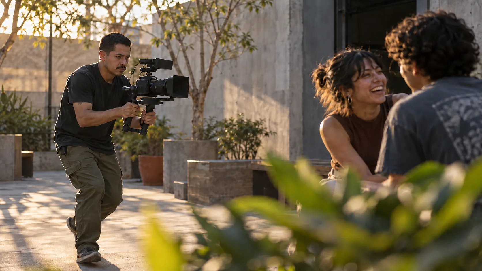 A videographer films two friends laughing as he moves through a courtyard.