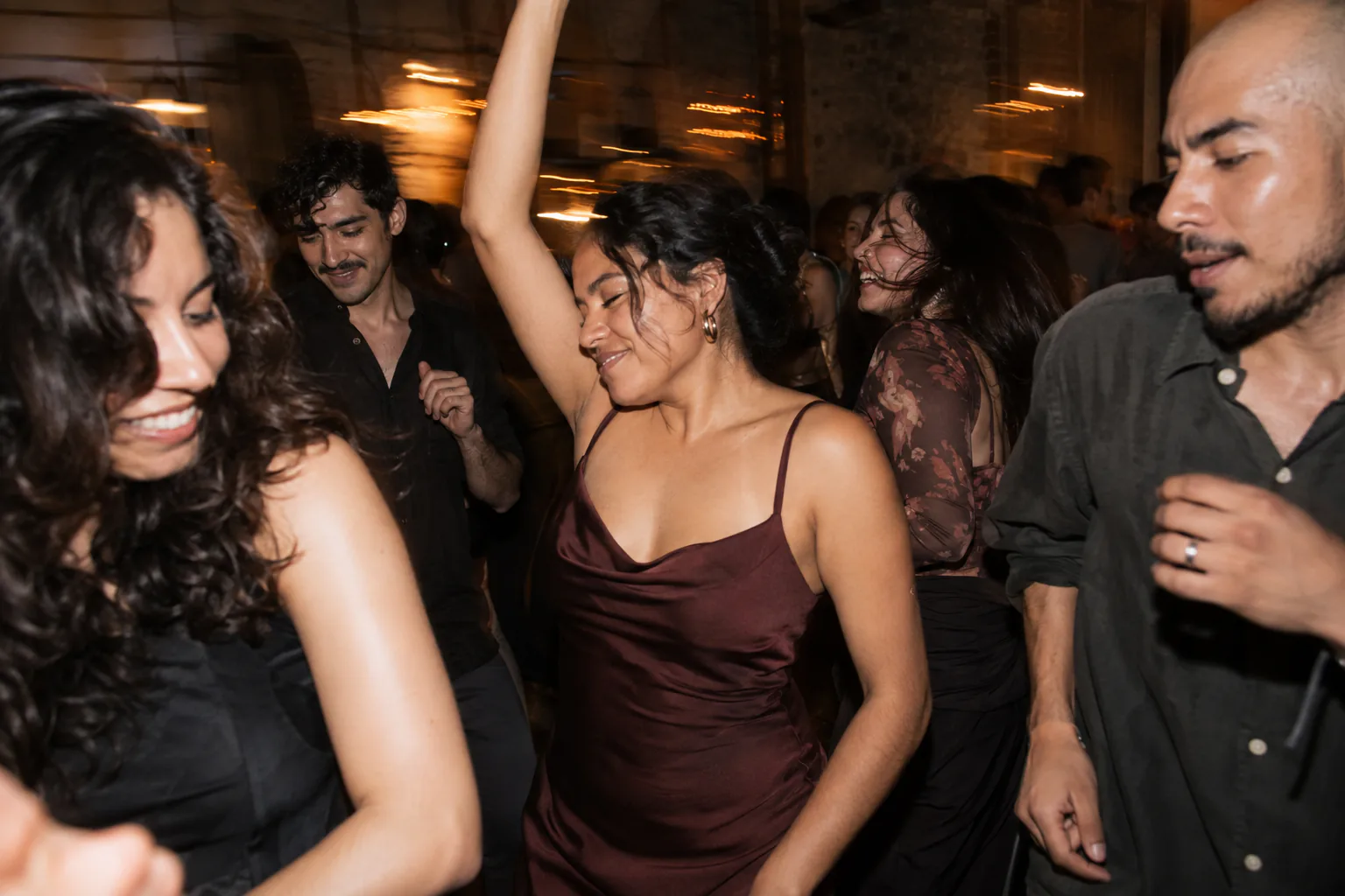 Friends dancing and laughing on a dance floor at night, among moving lights.